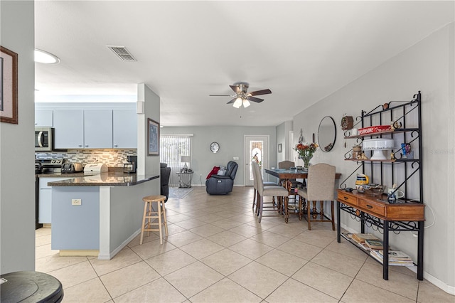 kitchen with a kitchen breakfast bar, dark stone countertops, ceiling fan, white cabinets, and tasteful backsplash