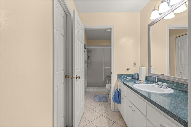 bathroom with a shower with door, vanity, toilet, and tile patterned floors