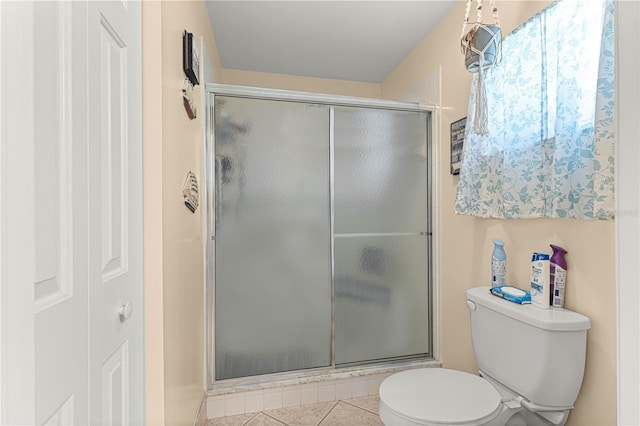 bathroom with a shower with door, toilet, and tile patterned floors