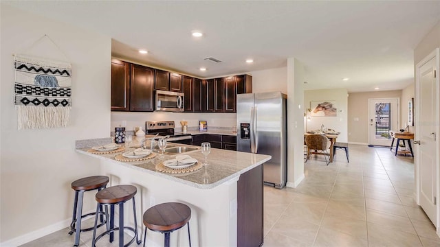 kitchen with light stone counters, light tile patterned floors, kitchen peninsula, stainless steel appliances, and a breakfast bar area