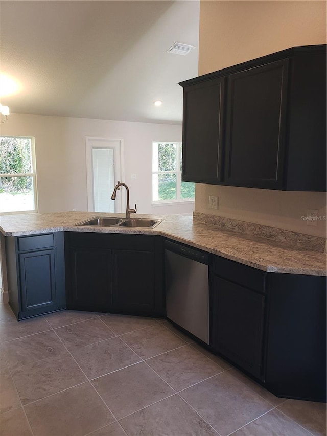 kitchen with stainless steel dishwasher, light tile patterned flooring, a sink, light stone countertops, and a peninsula