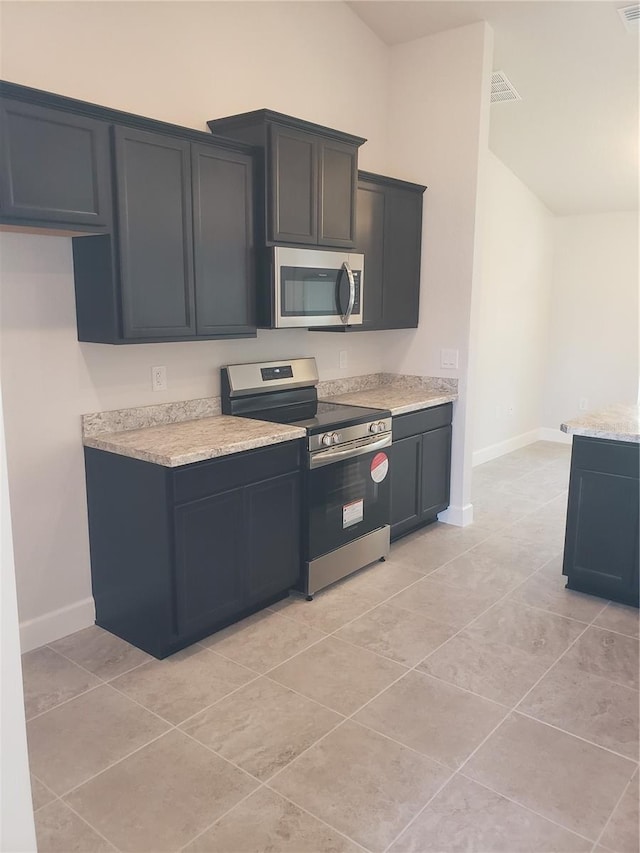 kitchen with baseboards, light stone counters, stainless steel appliances, and dark cabinetry