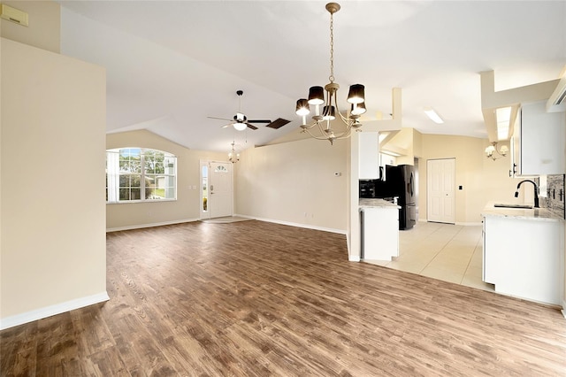 unfurnished living room with ceiling fan with notable chandelier, lofted ceiling, sink, and light hardwood / wood-style flooring