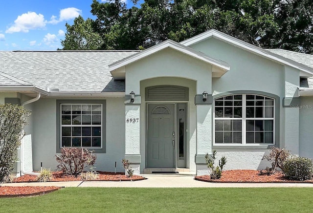 property entrance featuring a lawn, stucco siding, and a shingled roof