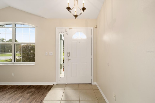 foyer entrance featuring a healthy amount of sunlight, baseboards, vaulted ceiling, and a notable chandelier