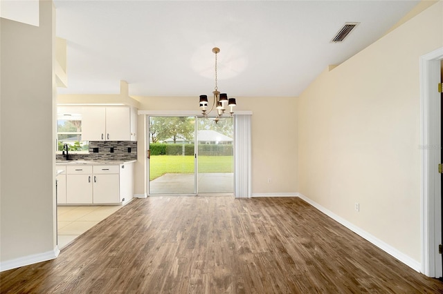 unfurnished dining area with visible vents, baseboards, wood finished floors, and an inviting chandelier