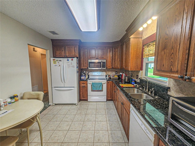 kitchen featuring light tile patterned floors, sink, white appliances, tasteful backsplash, and dark stone counters