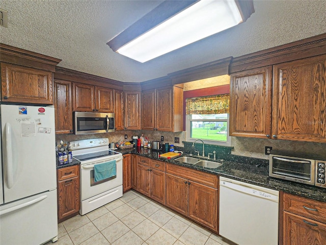 kitchen featuring dark stone countertops, light tile patterned flooring, sink, and white appliances