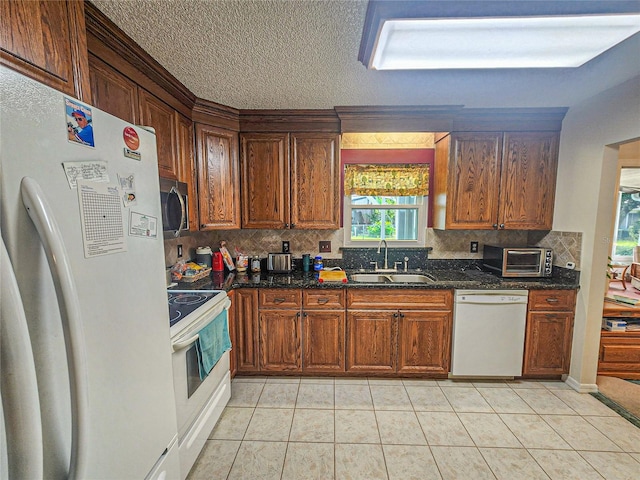 kitchen with dark stone countertops, white appliances, sink, light tile patterned flooring, and backsplash