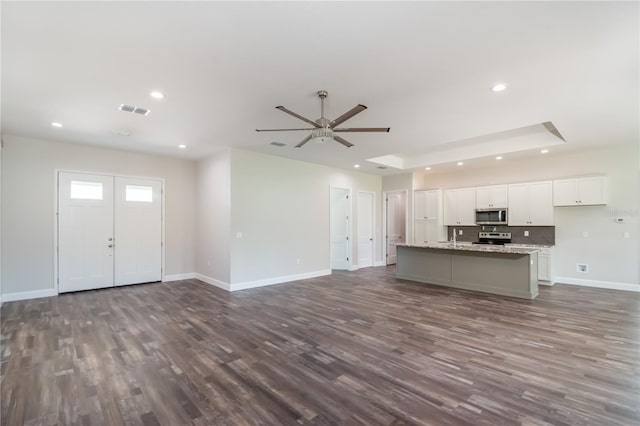 kitchen with a center island with sink, light stone counters, white cabinetry, dark wood-type flooring, and stainless steel appliances