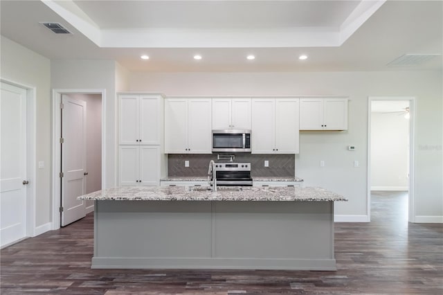 kitchen with a center island with sink, appliances with stainless steel finishes, light stone countertops, and white cabinetry