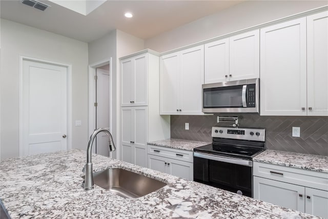 2073 NW 79th Loop, Ocala, FL 34475 - kitchen with stainless steel appliances, a sink, tasteful backsplash, white cabinets, and light stone counters