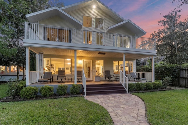 back house at dusk featuring a balcony, a patio, and a yard