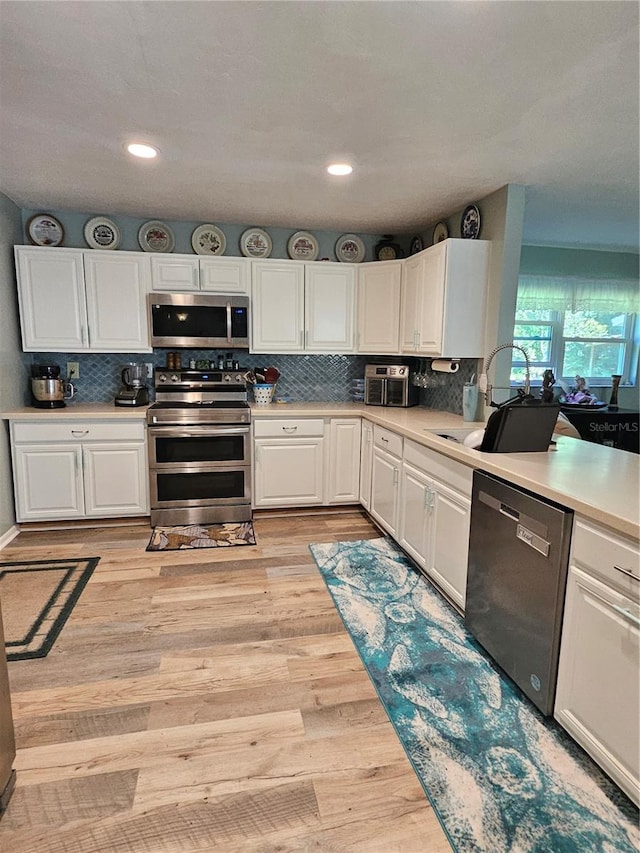 kitchen featuring appliances with stainless steel finishes, light wood-type flooring, sink, and white cabinets