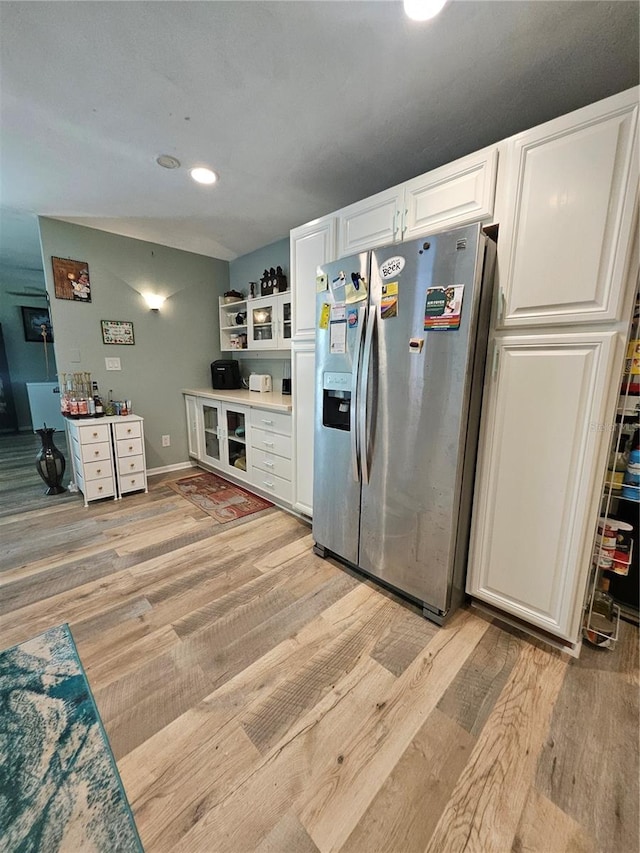 kitchen with white cabinets, stainless steel fridge with ice dispenser, light hardwood / wood-style flooring, and vaulted ceiling