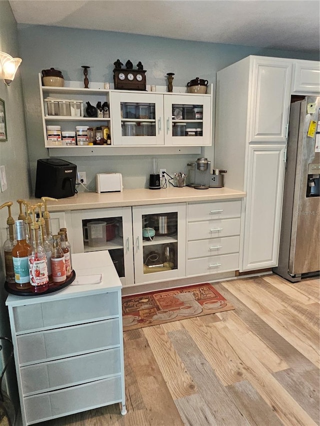 bar featuring white cabinetry, light hardwood / wood-style floors, and stainless steel refrigerator with ice dispenser