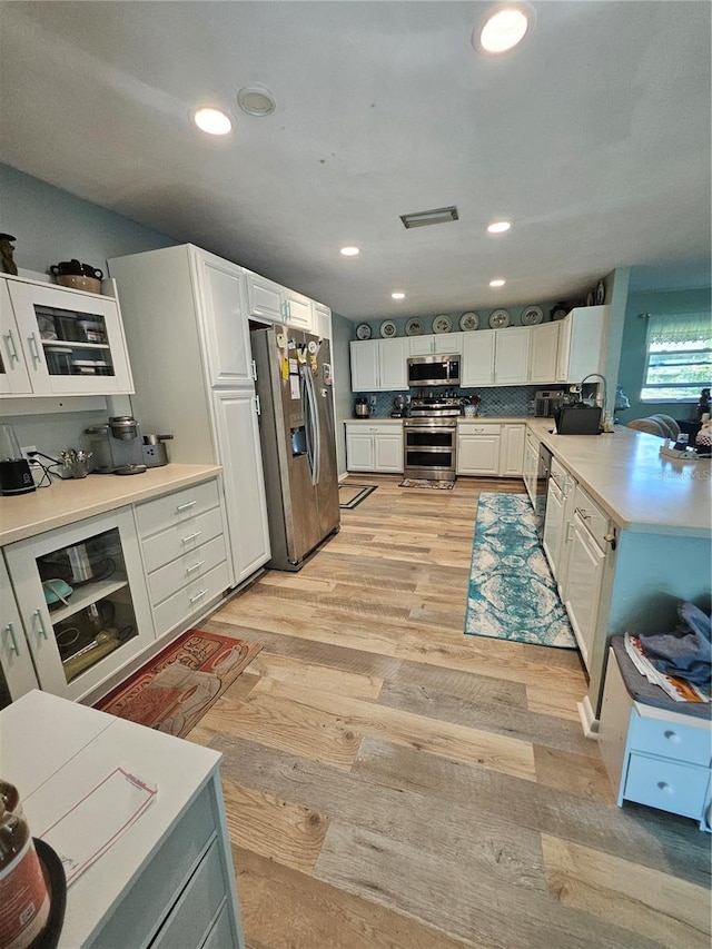 kitchen with decorative backsplash, stainless steel appliances, sink, white cabinetry, and light hardwood / wood-style flooring