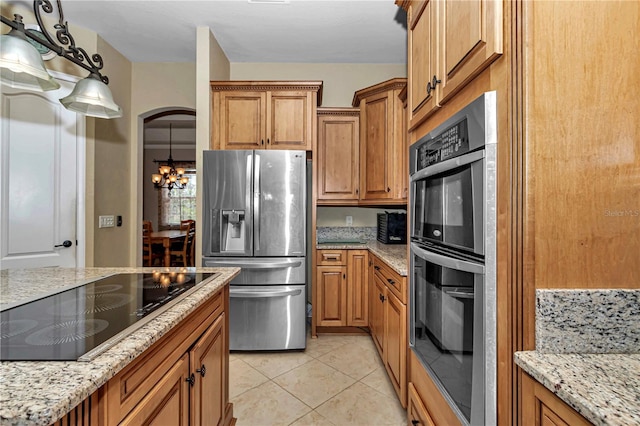 kitchen with light tile patterned flooring, stainless steel appliances, decorative light fixtures, light stone counters, and an inviting chandelier