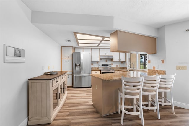 kitchen with kitchen peninsula, appliances with stainless steel finishes, a kitchen bar, sink, and light hardwood / wood-style floors