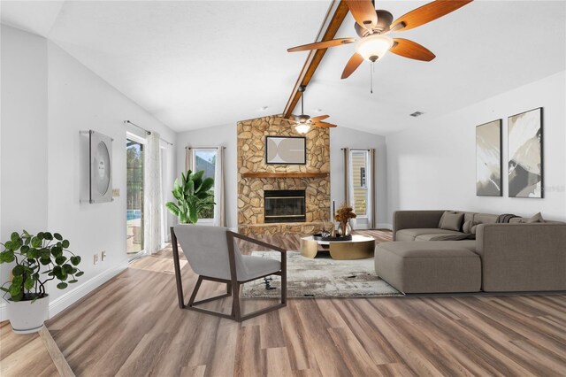 living room featuring hardwood / wood-style flooring, lofted ceiling with beams, ceiling fan, and a stone fireplace