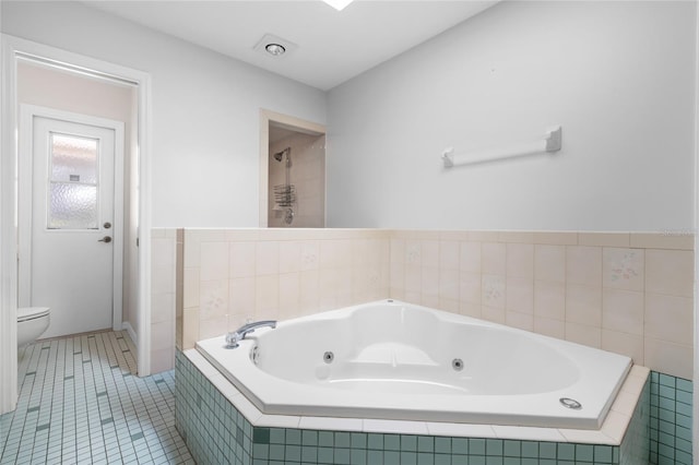 bathroom featuring tile patterned flooring, a relaxing tiled tub, and toilet