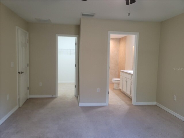 unfurnished bedroom featuring a spacious closet, light carpet, ensuite bathroom, and baseboards