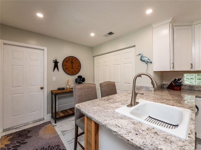 kitchen featuring light stone countertops, sink, and white cabinets