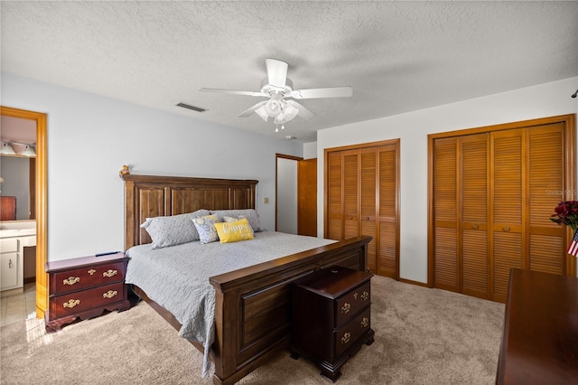 carpeted bedroom featuring ceiling fan, a textured ceiling, and two closets