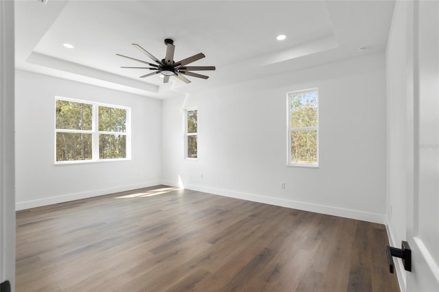 empty room featuring a tray ceiling, ceiling fan, and dark hardwood / wood-style flooring