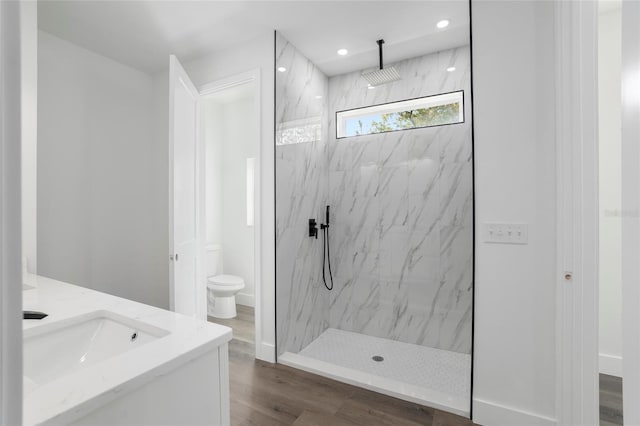 bathroom with toilet, hardwood / wood-style floors, vanity, and a tile shower