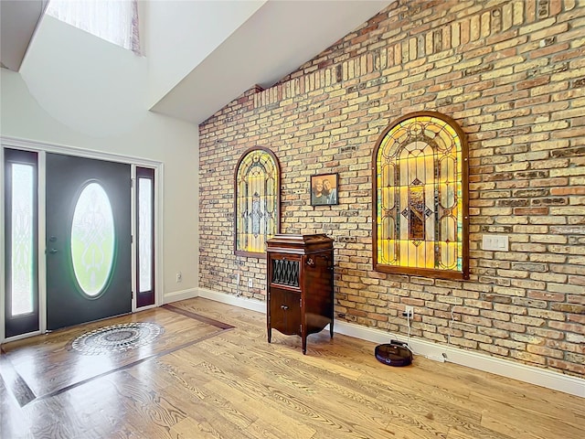 foyer featuring high vaulted ceiling, brick wall, and light wood-type flooring