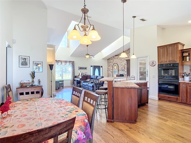 dining room featuring sink, high vaulted ceiling, light hardwood / wood-style flooring, and ceiling fan with notable chandelier