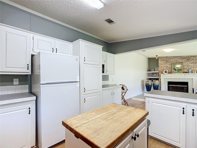 kitchen featuring white fridge, light hardwood / wood-style flooring, a fireplace, and white cabinets