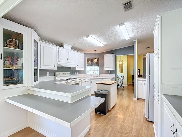 kitchen with kitchen peninsula, decorative light fixtures, white cabinets, a textured ceiling, and white appliances