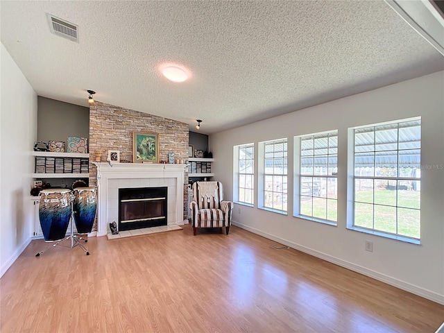 unfurnished living room featuring light hardwood / wood-style flooring, a textured ceiling, lofted ceiling, and a fireplace