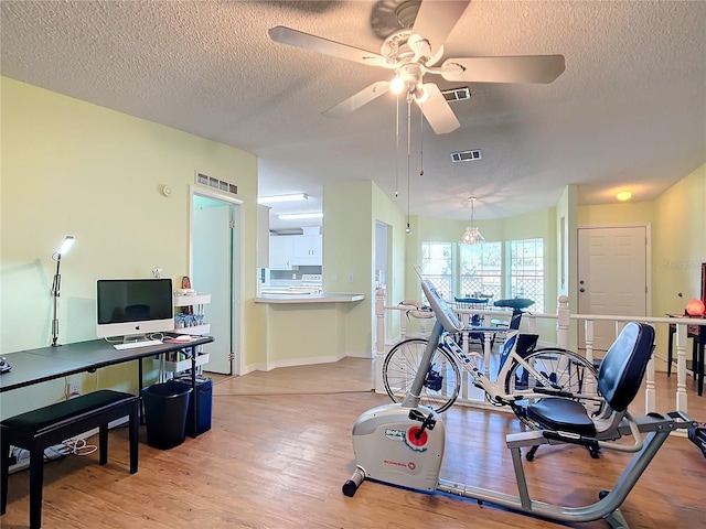 exercise room featuring a textured ceiling, light wood-type flooring, and ceiling fan