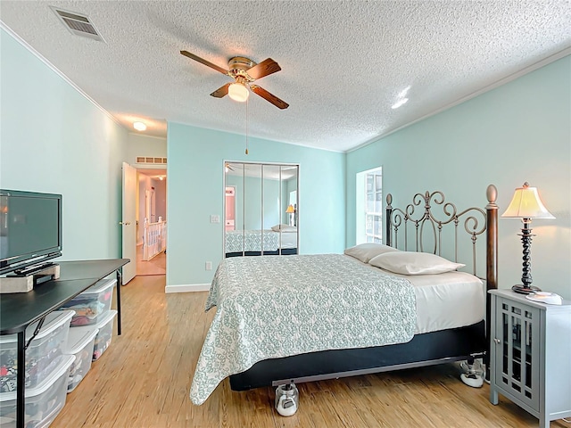 bedroom with a closet, light hardwood / wood-style flooring, ornamental molding, a textured ceiling, and ceiling fan