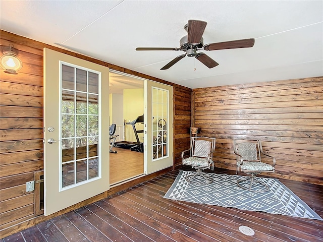 sitting room featuring dark wood-type flooring, wooden walls, and ceiling fan