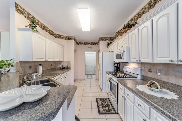 kitchen featuring backsplash, sink, light tile patterned flooring, stainless steel gas range oven, and white cabinets