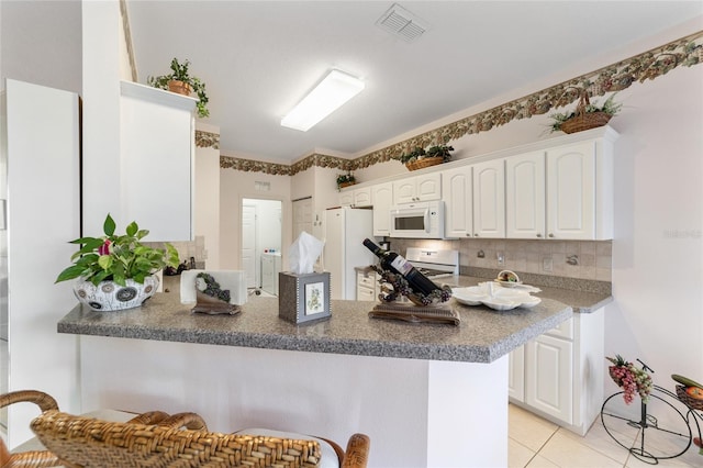 kitchen with white appliances, backsplash, kitchen peninsula, white cabinetry, and light tile patterned floors