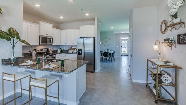 kitchen featuring white cabinets, kitchen peninsula, dark stone counters, appliances with stainless steel finishes, and a kitchen bar