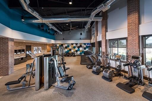 exercise room with carpet floors, a towering ceiling, and brick wall