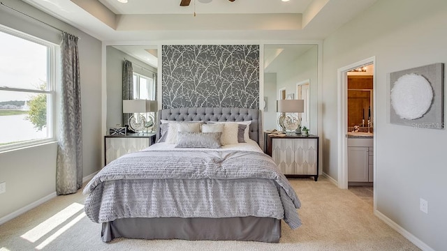 carpeted bedroom featuring a raised ceiling, ceiling fan, sink, and ensuite bath