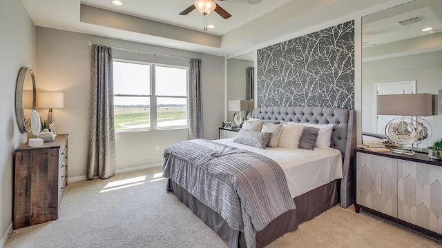 bedroom featuring ceiling fan, light colored carpet, and a tray ceiling