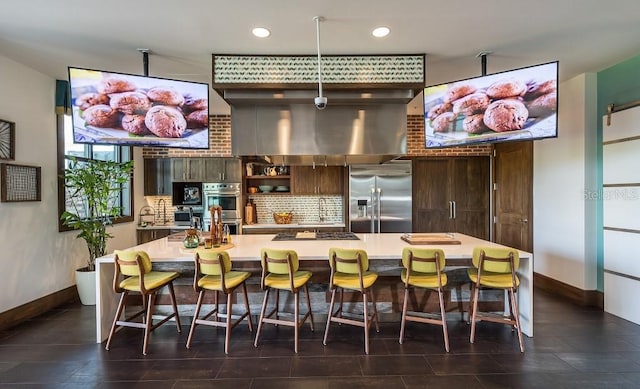 kitchen with dark brown cabinetry, a kitchen island with sink, decorative backsplash, stainless steel appliances, and a kitchen breakfast bar