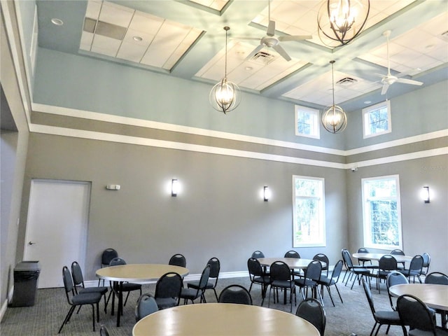 dining room with a towering ceiling, ceiling fan with notable chandelier, carpet floors, and coffered ceiling