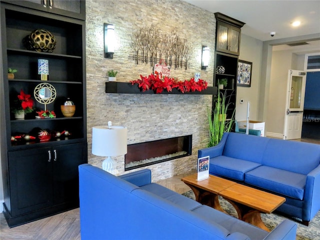 living room featuring built in shelves, light parquet flooring, and a stone fireplace