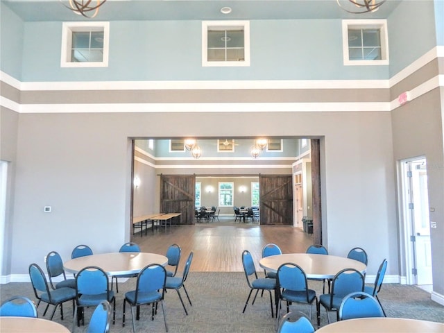 dining area with wood-type flooring, a barn door, and a high ceiling