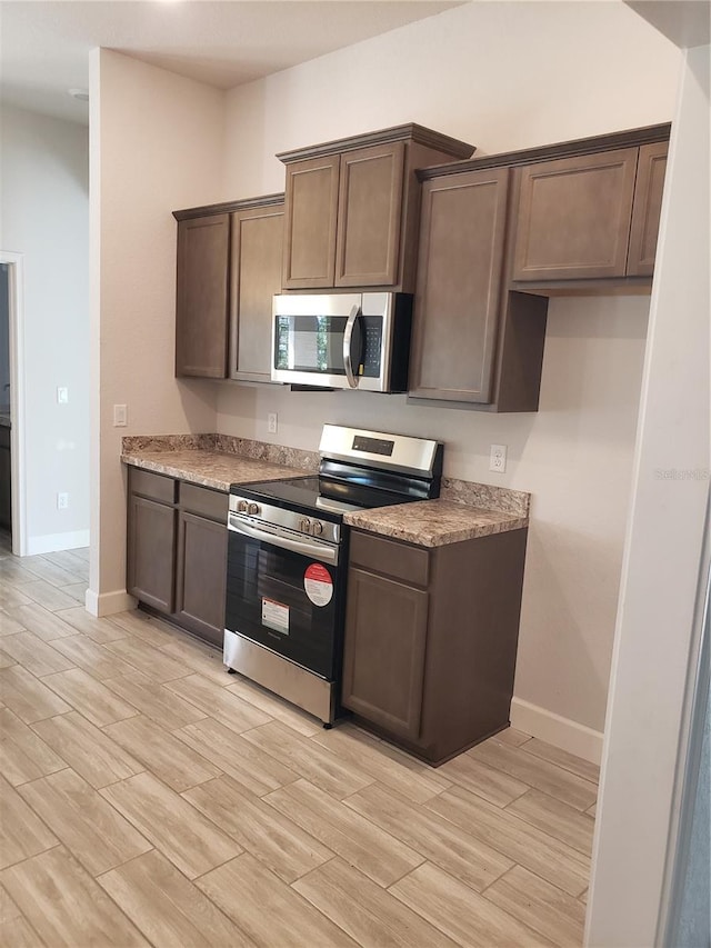 kitchen featuring appliances with stainless steel finishes, light stone counters, and dark brown cabinets