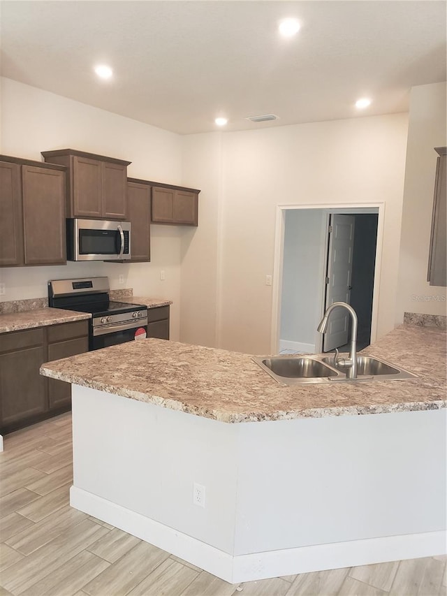 kitchen with kitchen peninsula, light stone counters, appliances with stainless steel finishes, light hardwood / wood-style floors, and sink